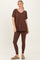 woman wearing a brown oversized v-neck top with rolled sleeves and matching brown leggings, styled with tan slip-on shoes