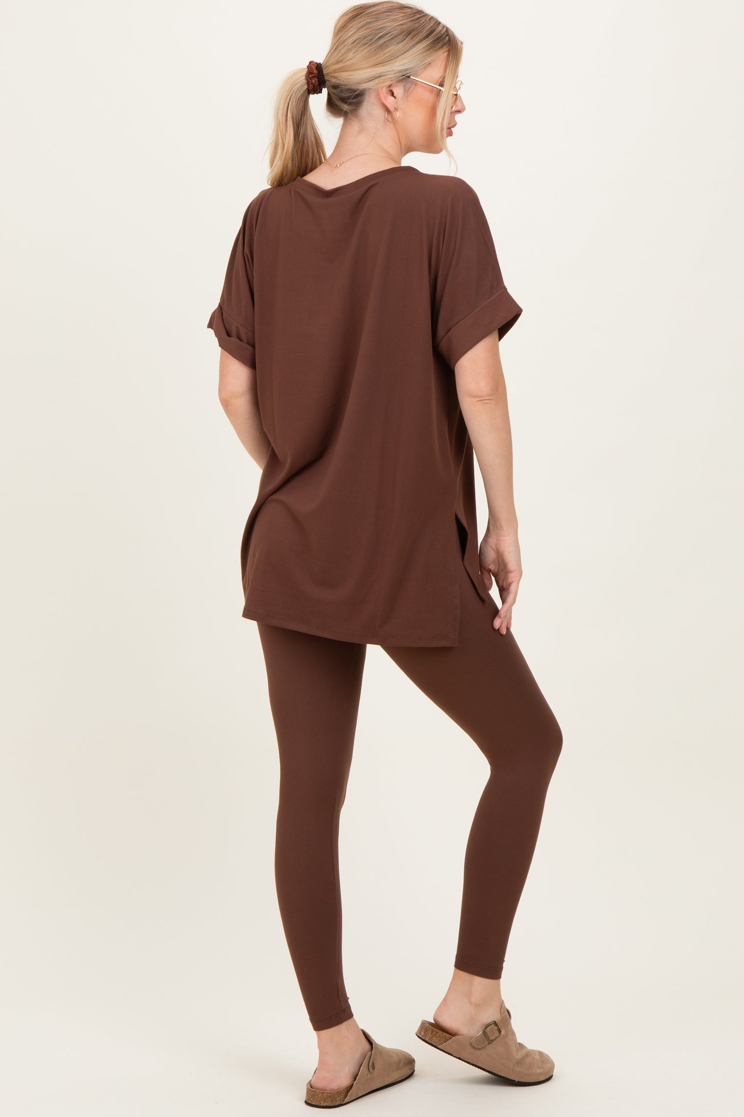 woman wearing a brown oversized t-shirt paired with brown leggings and slip-on sandals from a rear angle