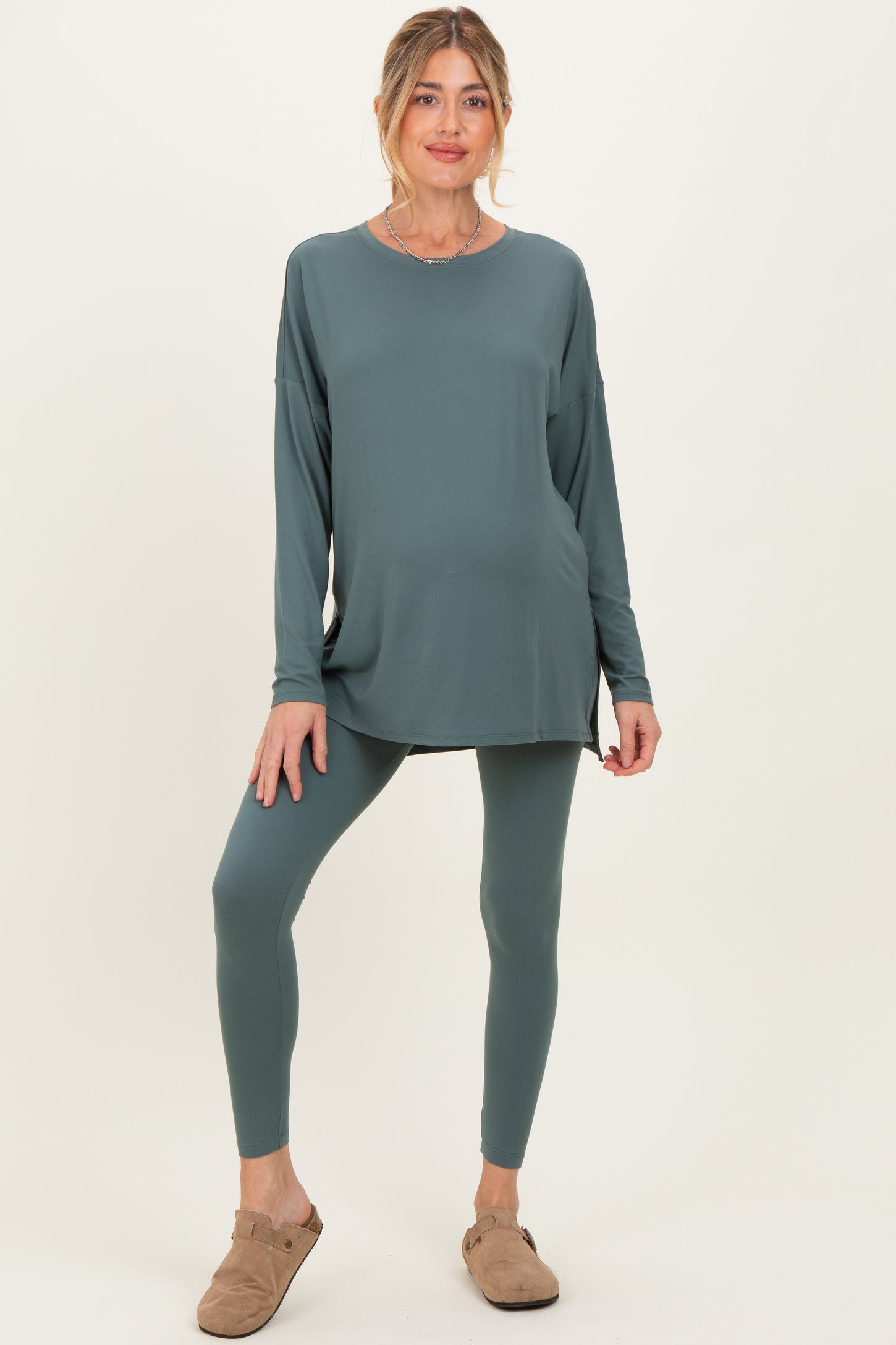 woman wearing a teal long sleeve maternity top and matching leggings, standing with a relaxed pose