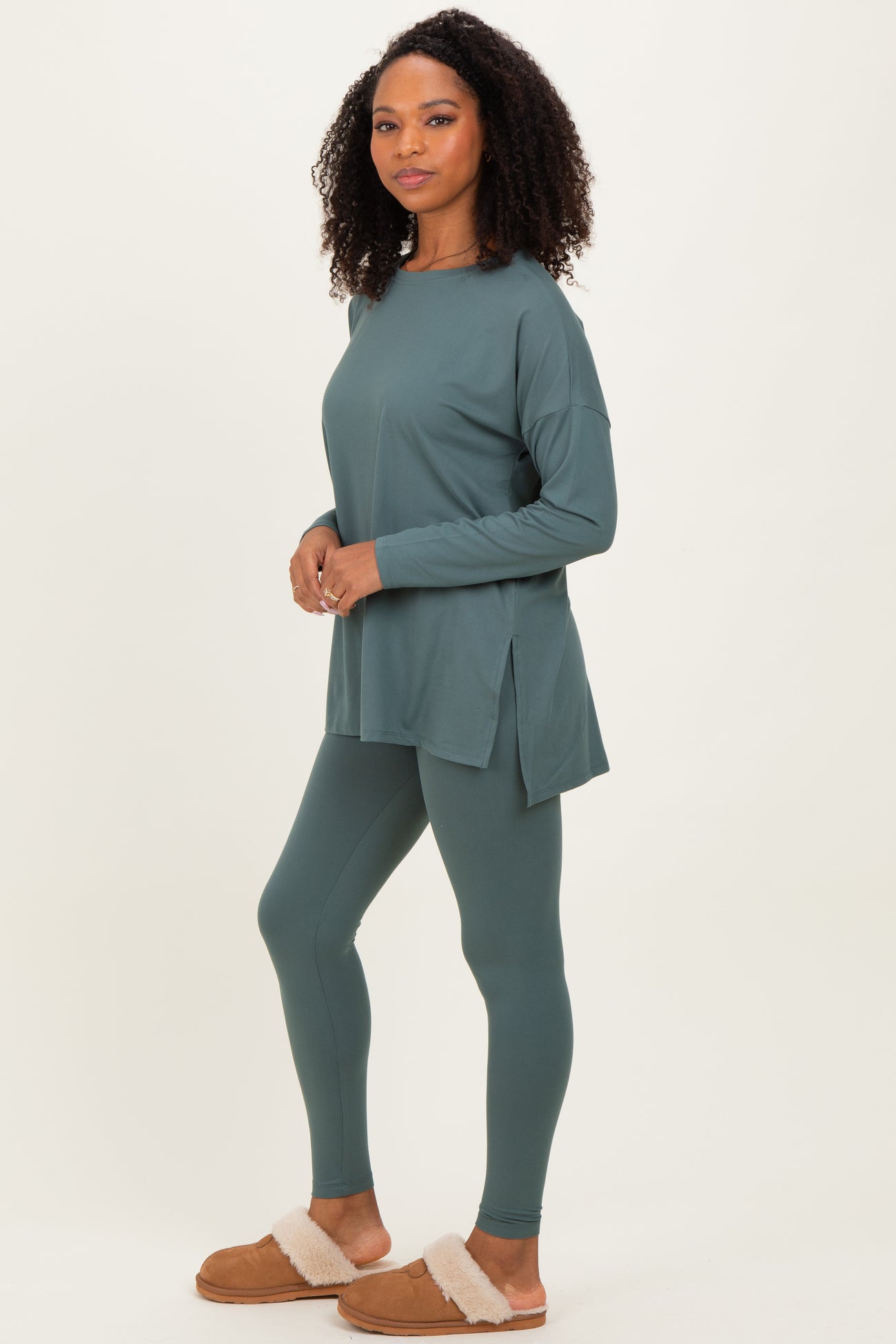 woman wearing a teal long sleeve tunic top and matching leggings with side slits, paired with cozy tan slippers