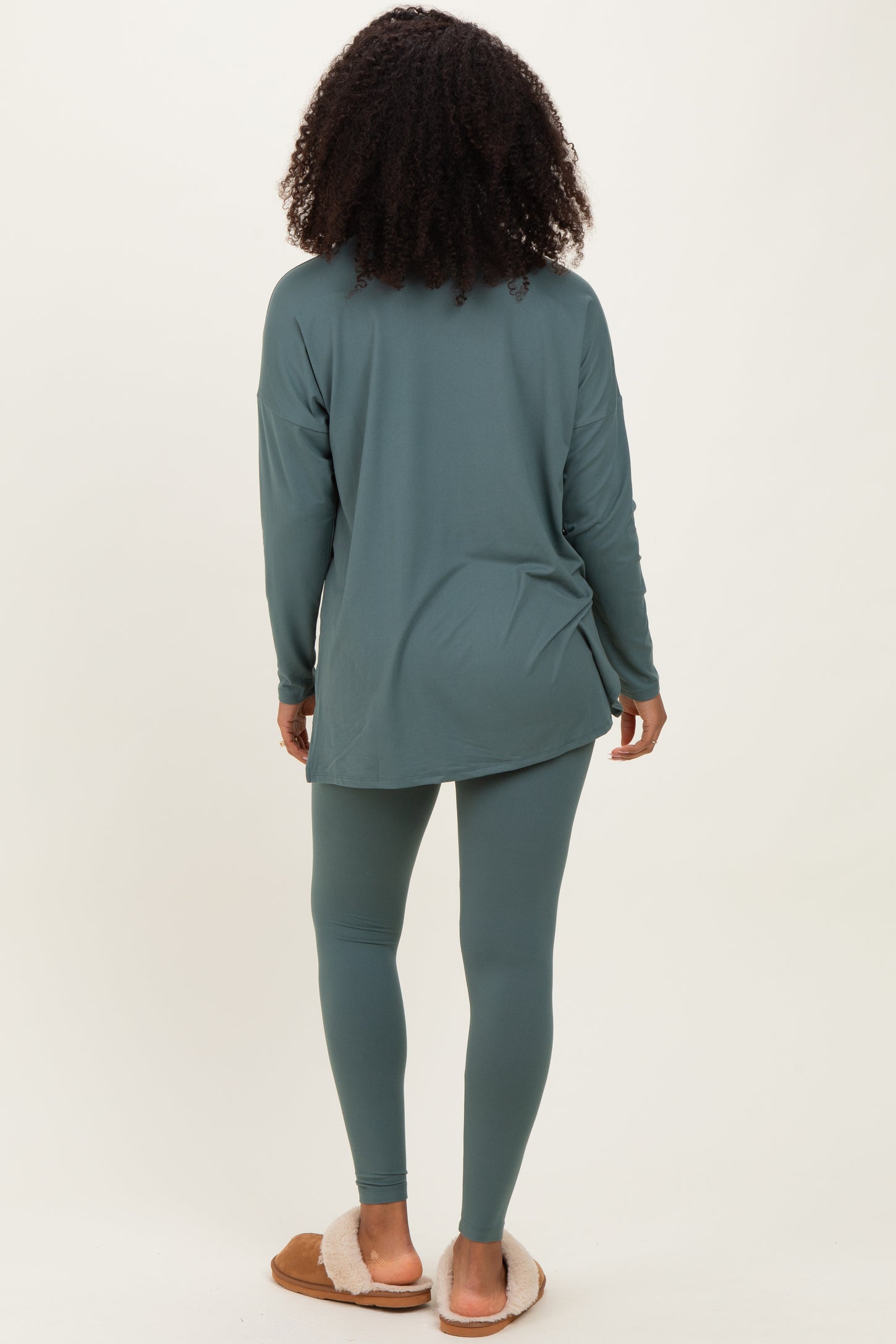 woman wearing a long sleeve teal tunic and matching leggings, seen from the back, paired with cozy slippers