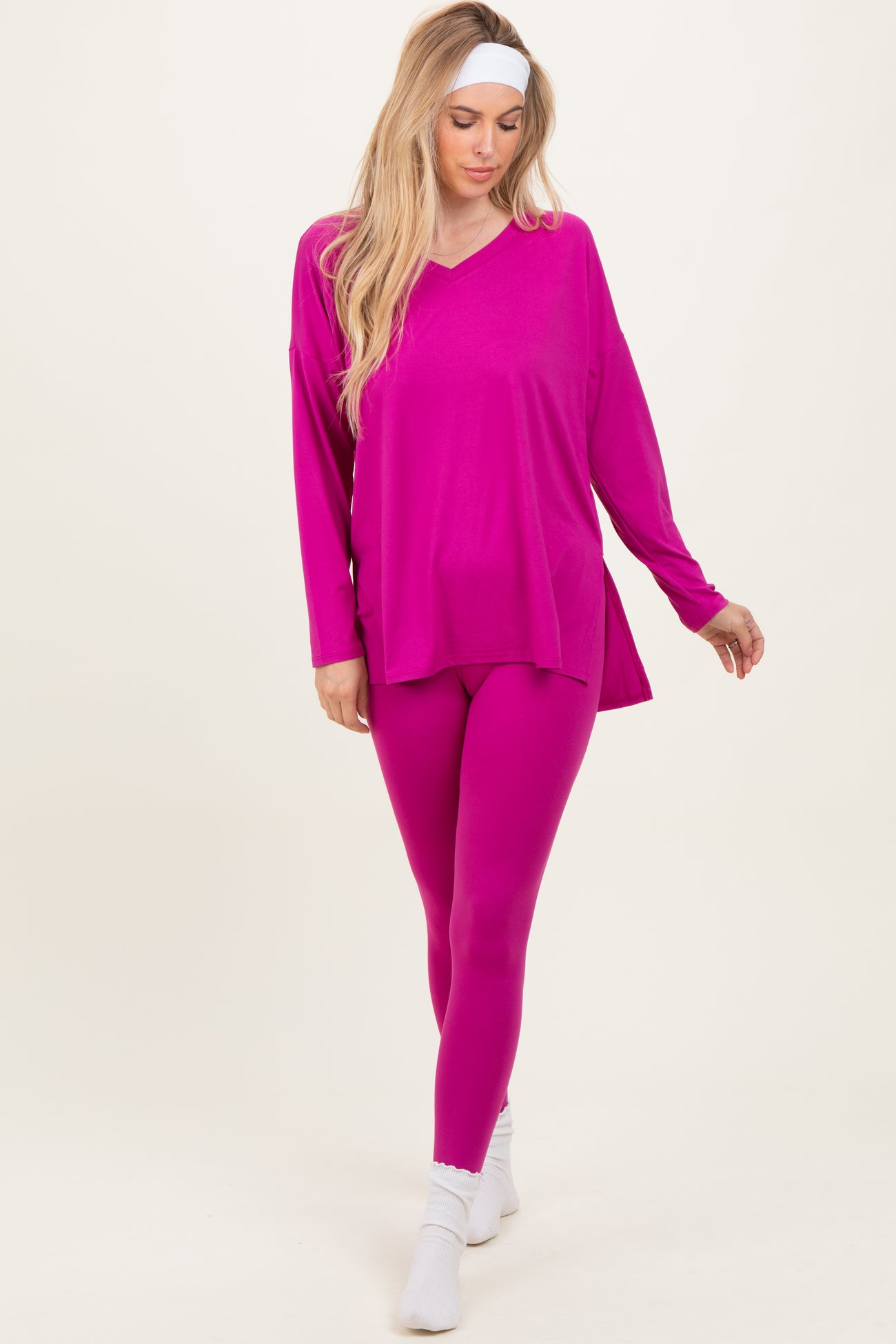 woman wearing a bright pink oversized v-neck top and matching leggings, styled with a white headband