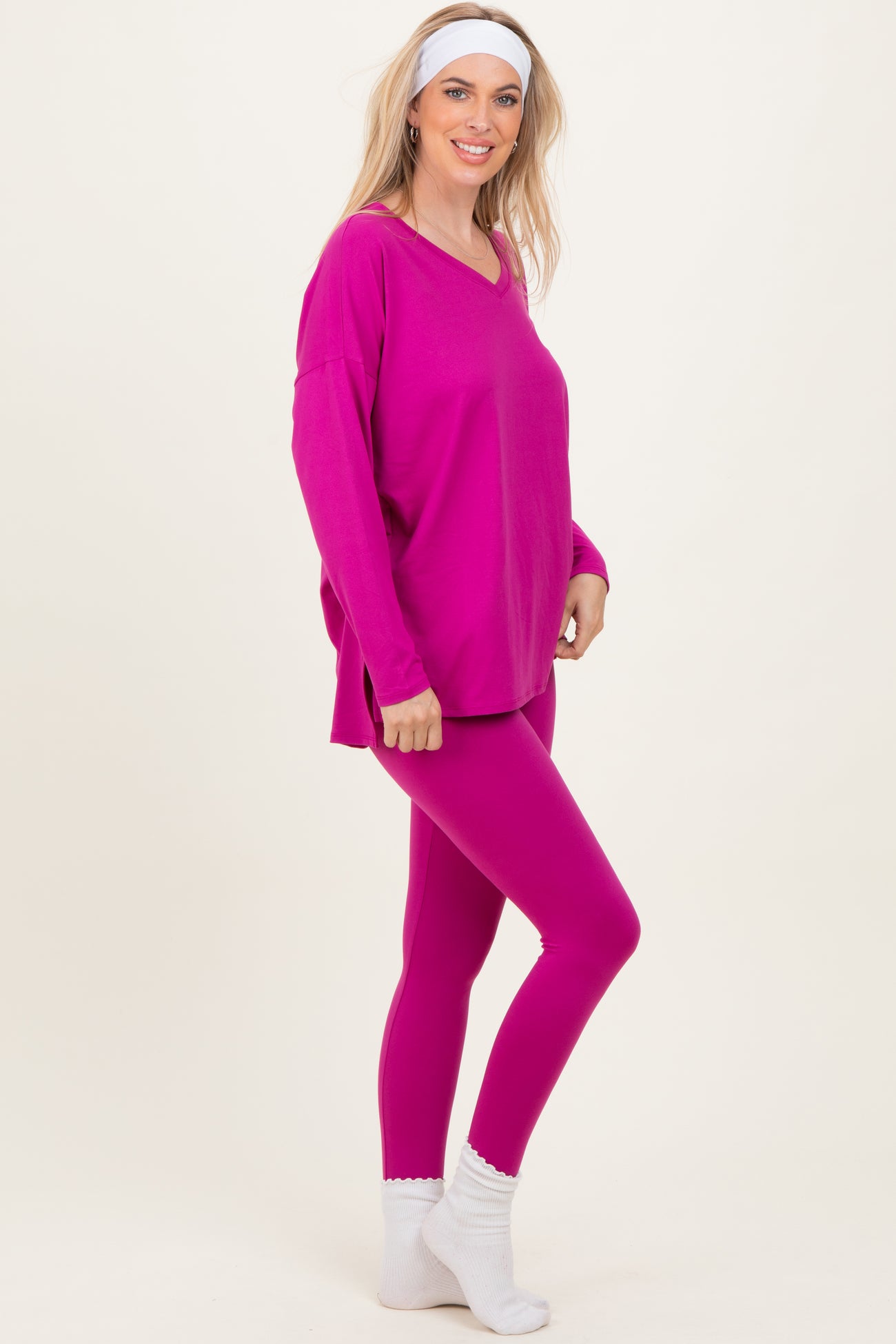 woman wearing a bright pink oversized v-neck top and matching pink leggings, styled with white ankle socks and a headband