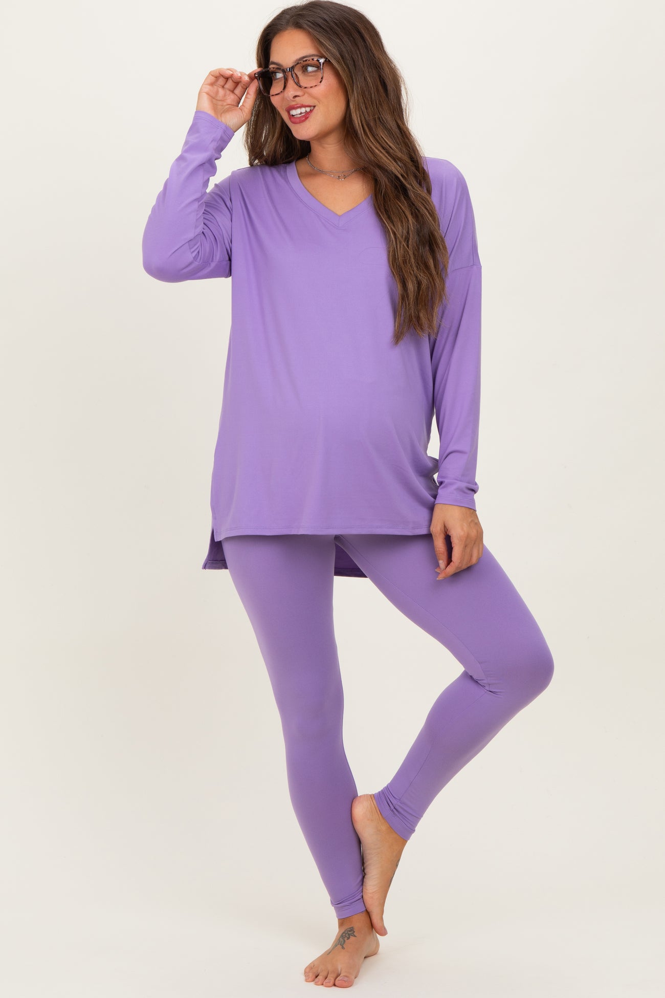 woman wearing a purple v-neck maternity top and matching leggings, showing her baby bump while smiling