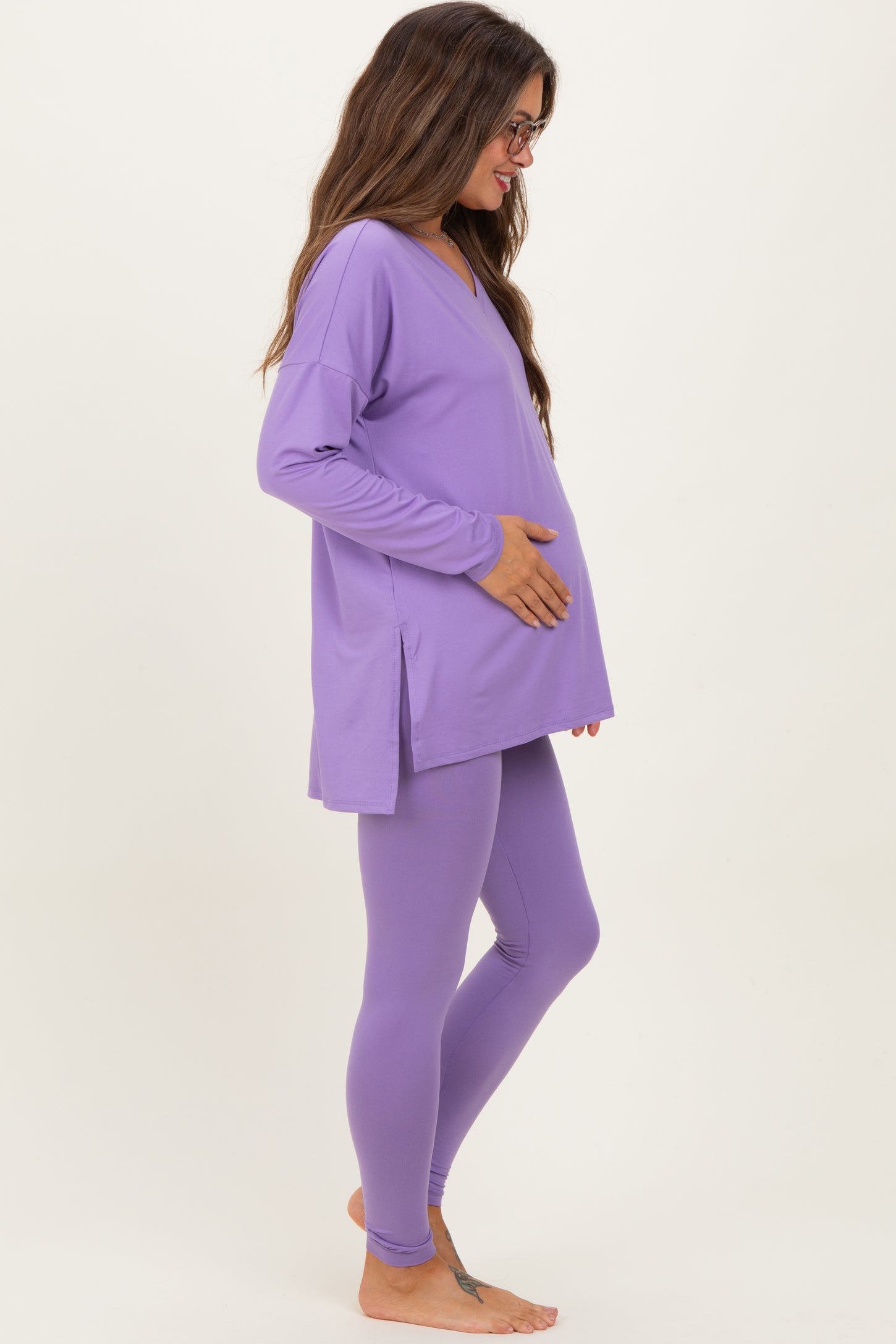 woman wearing a purple maternity top and leggings, gently holding her baby bump