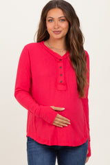 woman wearing a bright pink long sleeve maternity top with button details and holding her baby bump