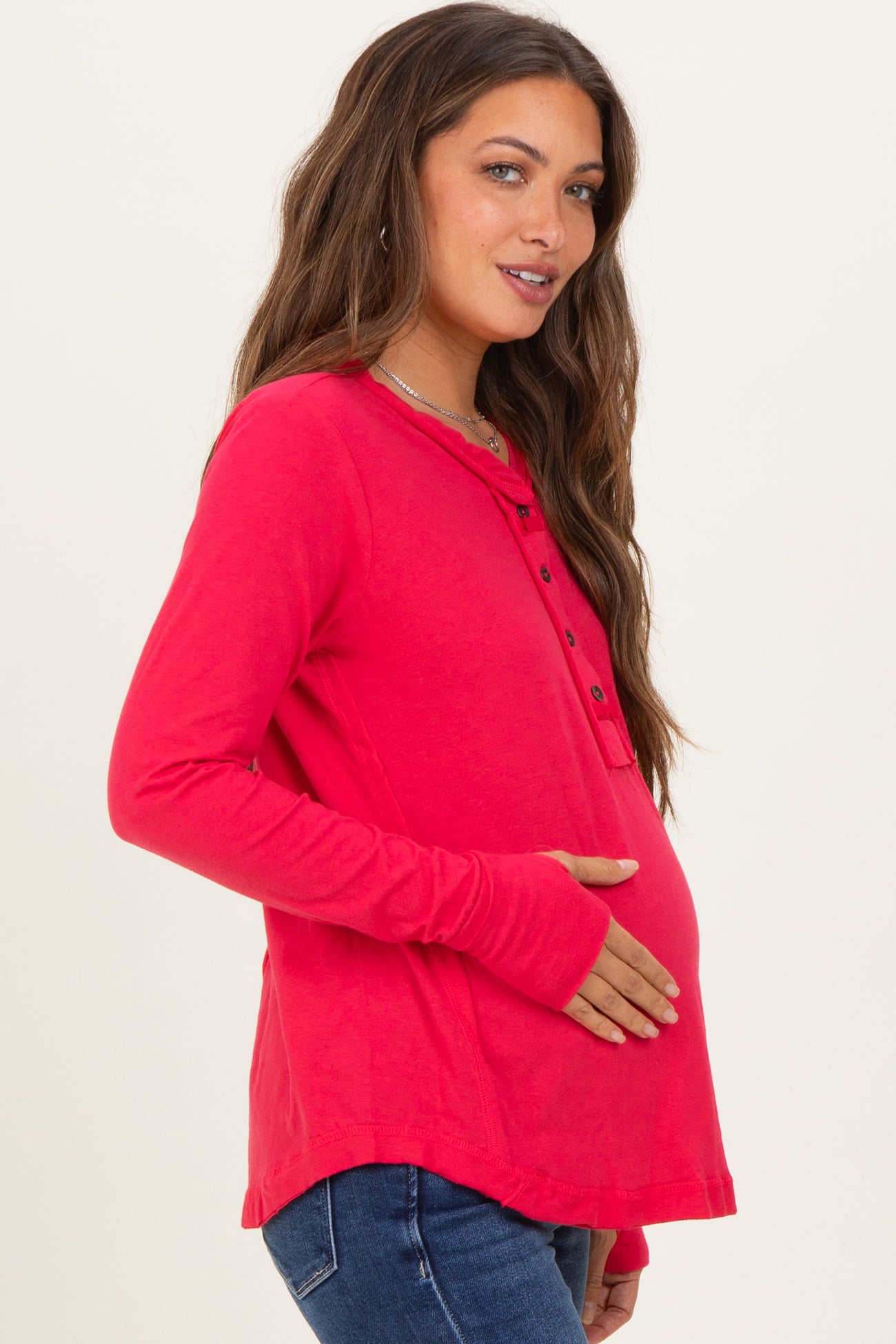 woman wearing a bright pink long sleeve maternity top and holding her baby bump