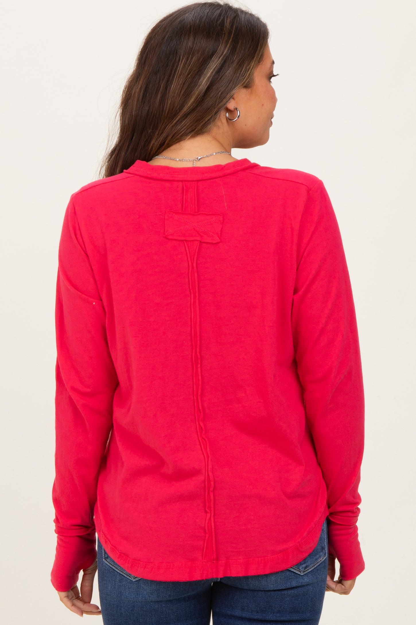 woman wearing a bright pink maternity long sleeve top showing a unique back design and casual fit