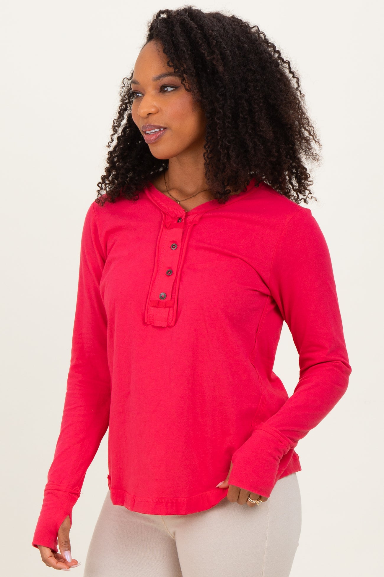 woman wearing a red long sleeve hooded top with button details and thumb holes, styled casually