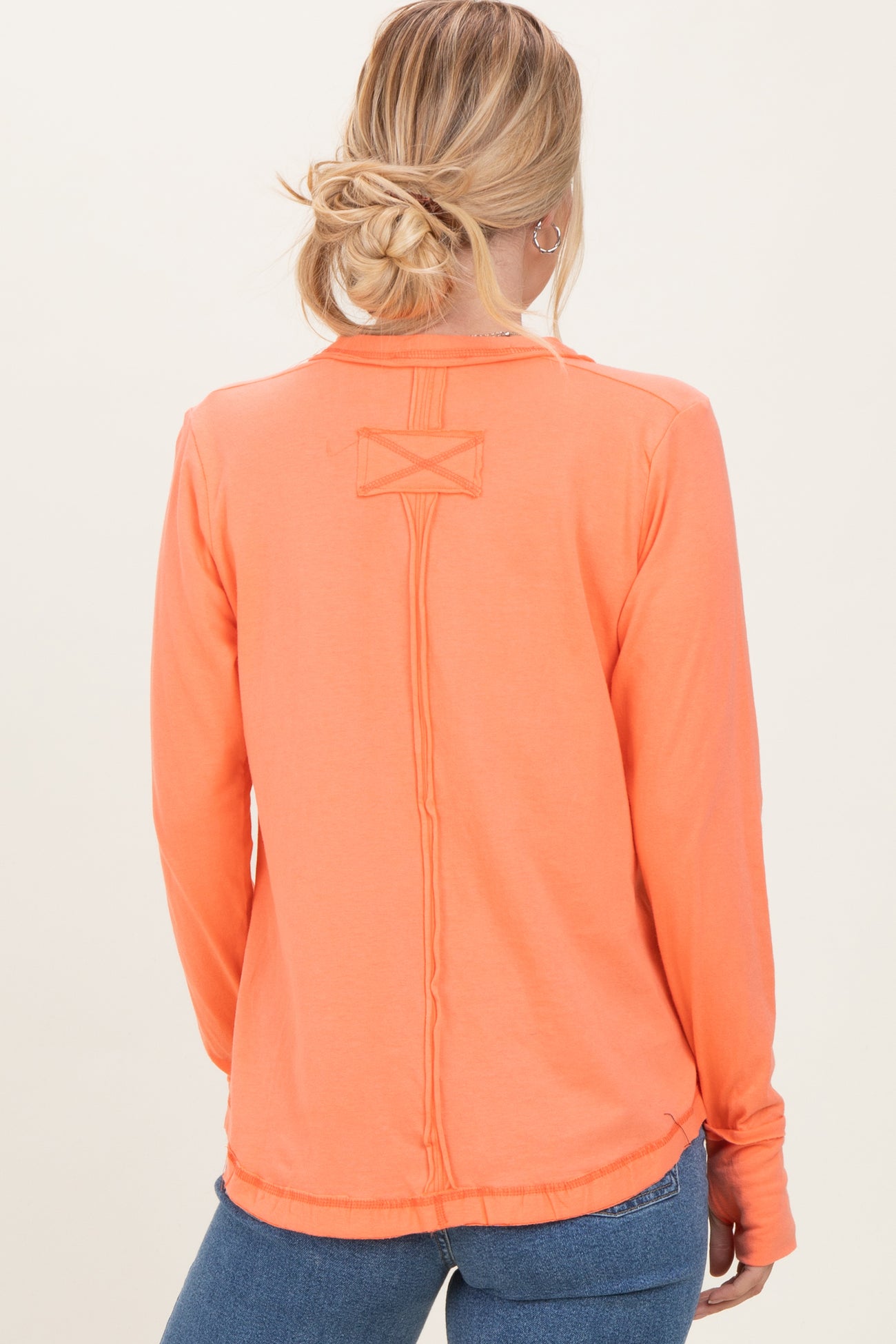 woman wearing an orange long sleeve top with a unique back stitch detail