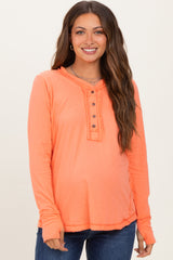 woman wearing an orange maternity long sleeve top with a henley neckline and front buttons, showing her baby bump