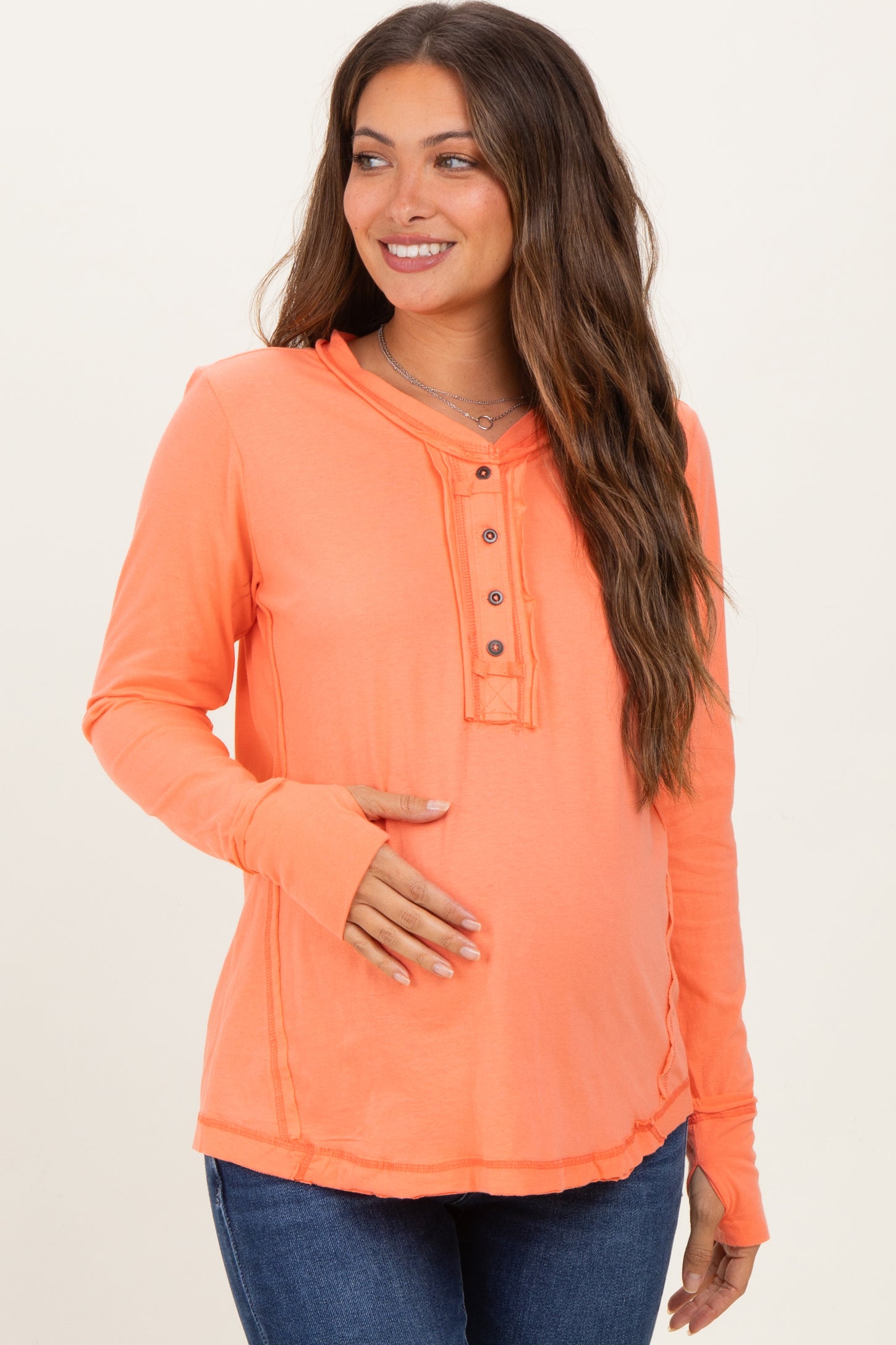 woman wearing a neon orange long sleeve maternity top with button details and a visible baby bump