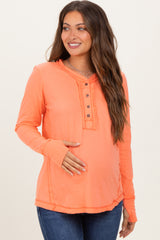 woman wearing a neon orange long sleeve maternity top with button details and a visible baby bump