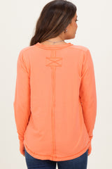 woman wearing a coral long sleeve maternity top with a decorative back detail and relaxed fit