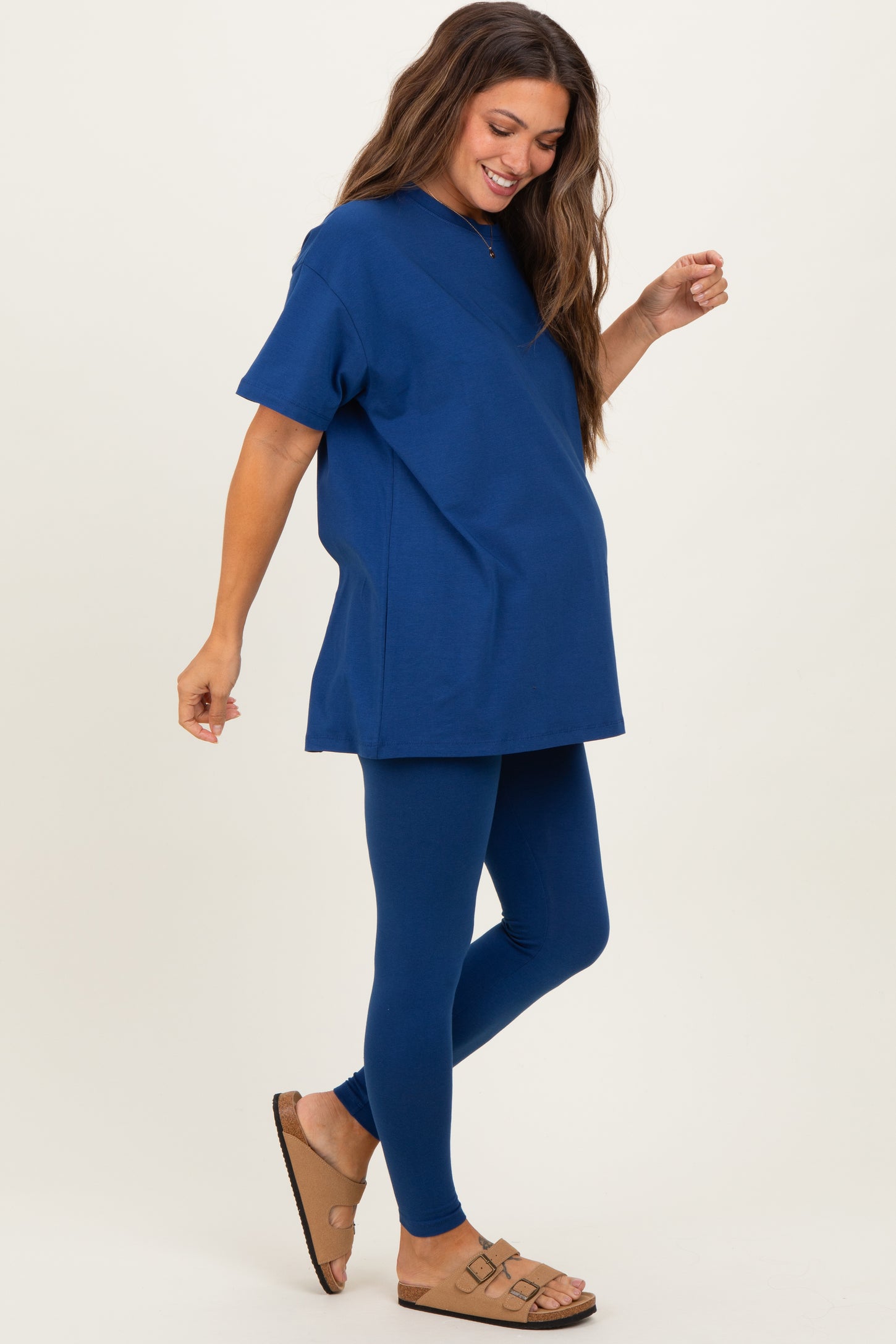 woman wearing a navy blue maternity t-shirt and matching leggings, showing her baby bump while standing and smiling