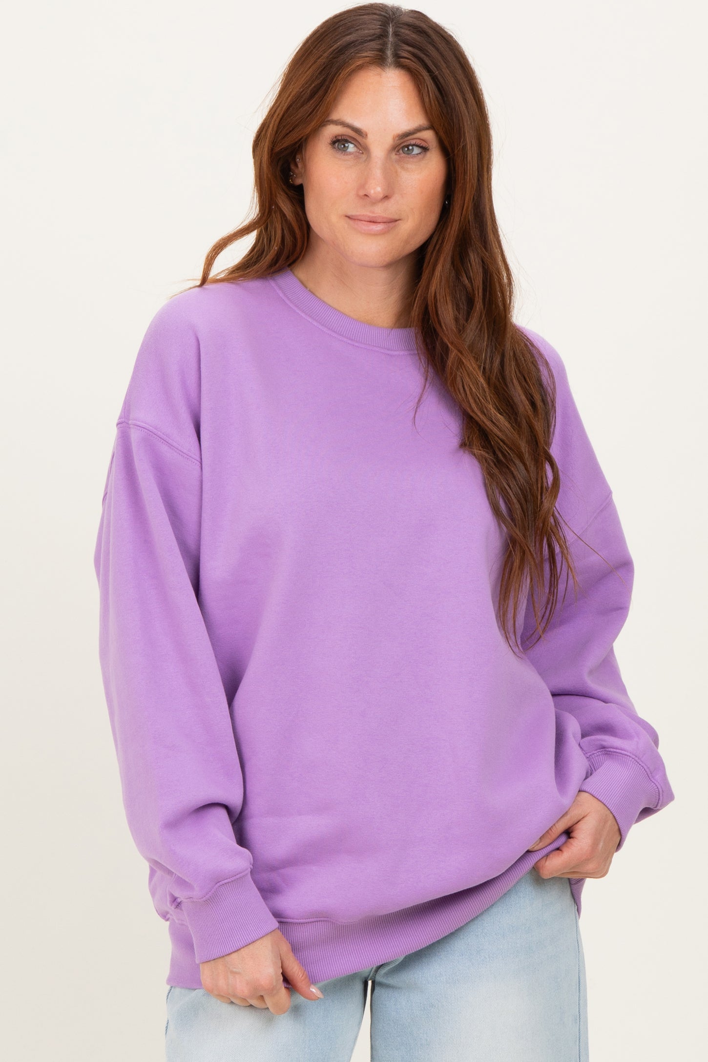 woman wearing a purple oversized sweatshirt with long sleeves and round neckline, posing against a neutral background