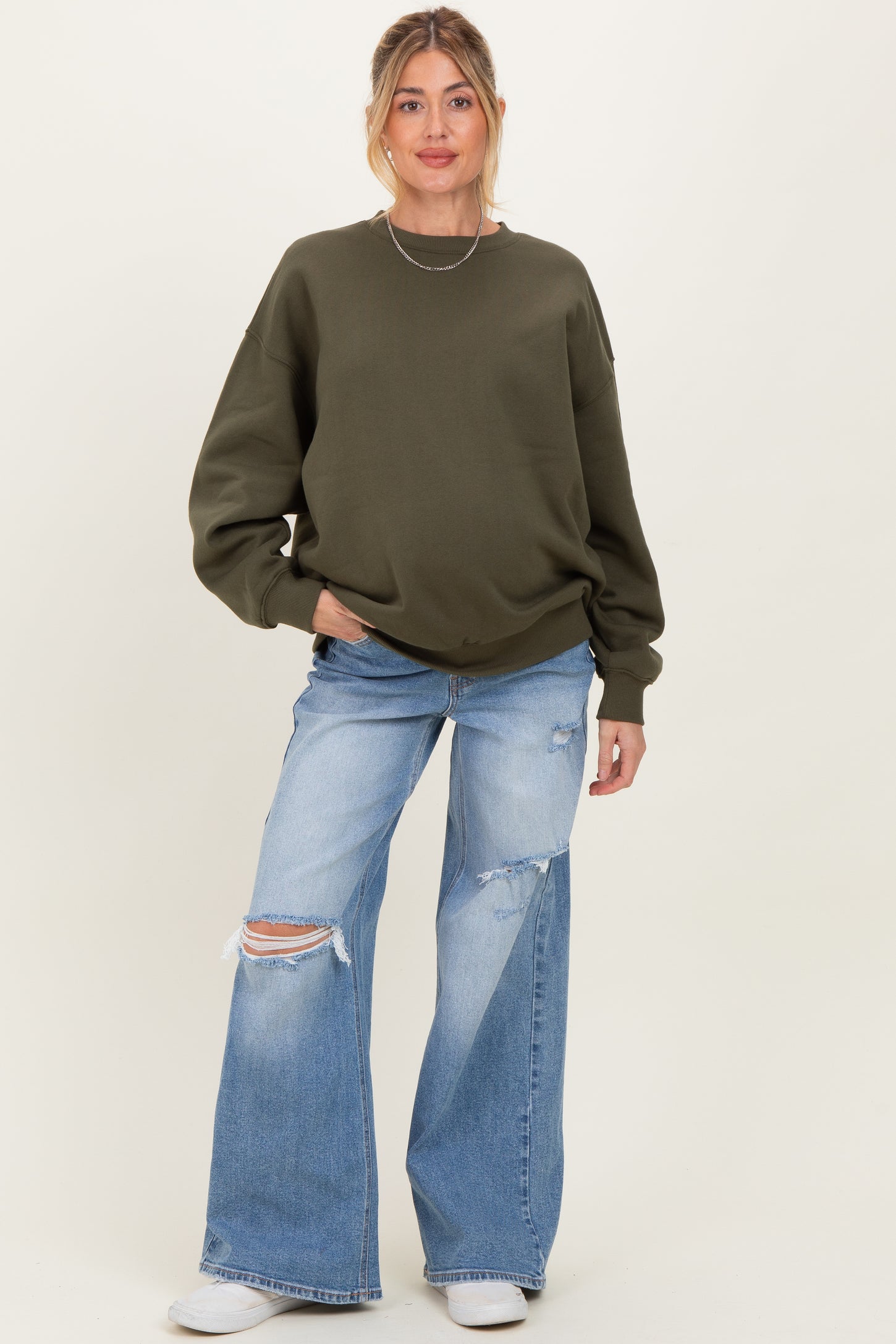 woman wearing an olive green oversized sweatshirt and distressed wide-leg jeans, showcasing her baby bump