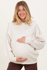 woman wearing a cream oversized maternity sweatshirt and holding her baby bump