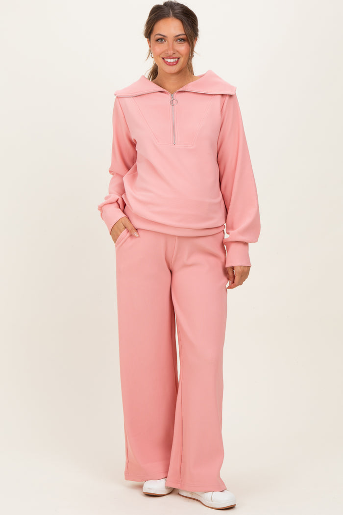 woman wearing a light pink ribbed maternity pullover with a collar and matching wide-leg pants, posing with hands in pockets