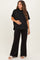 woman wearing a black maternity top and black wide-leg maternity pants, holding her baby bump