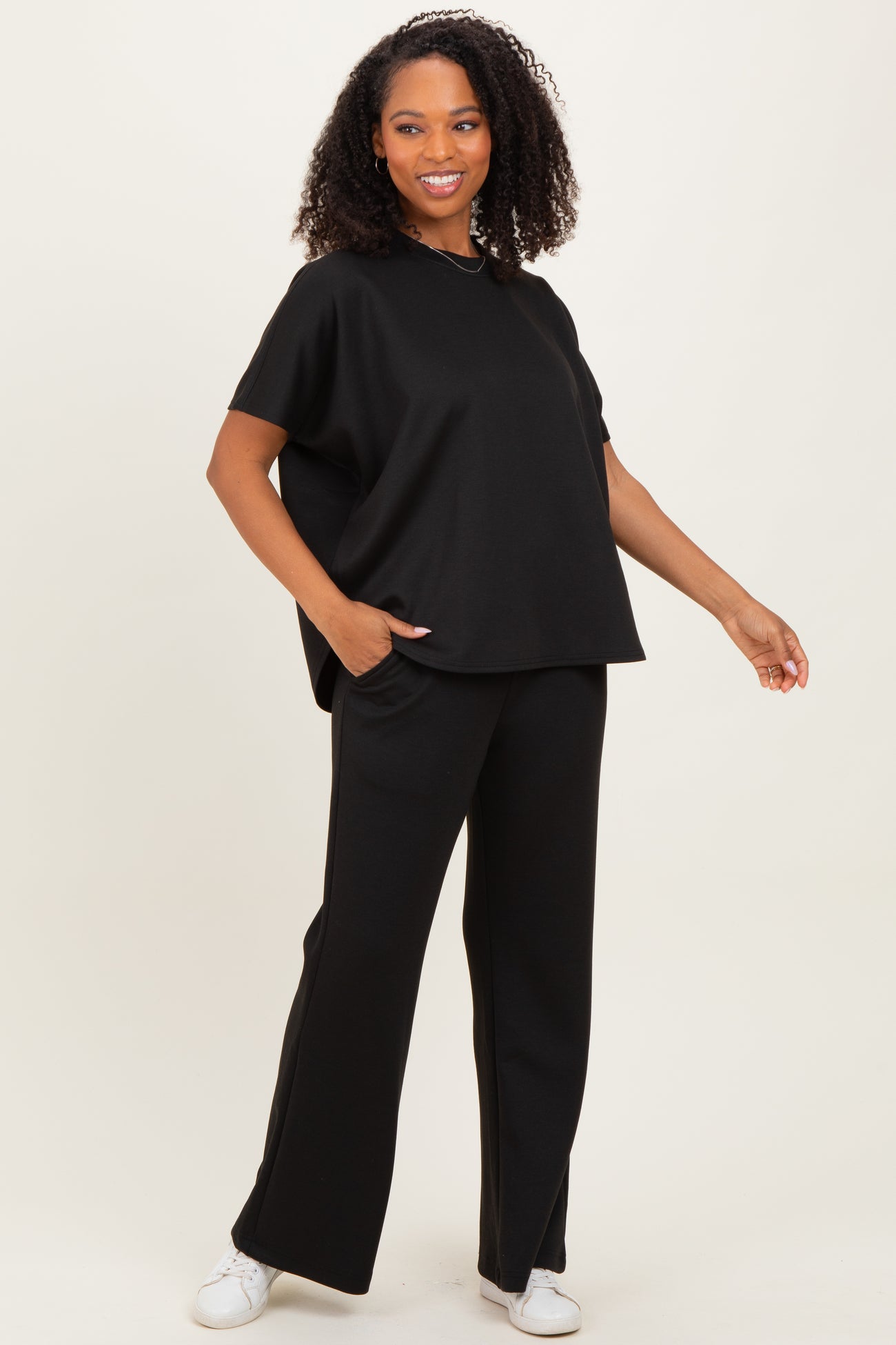 woman wearing a black short sleeve oversized top and black wide-leg pants, standing with one hand in her pocket