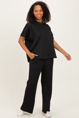 woman wearing a black short sleeve oversized top and black wide-leg pants, standing with one hand in her pocket