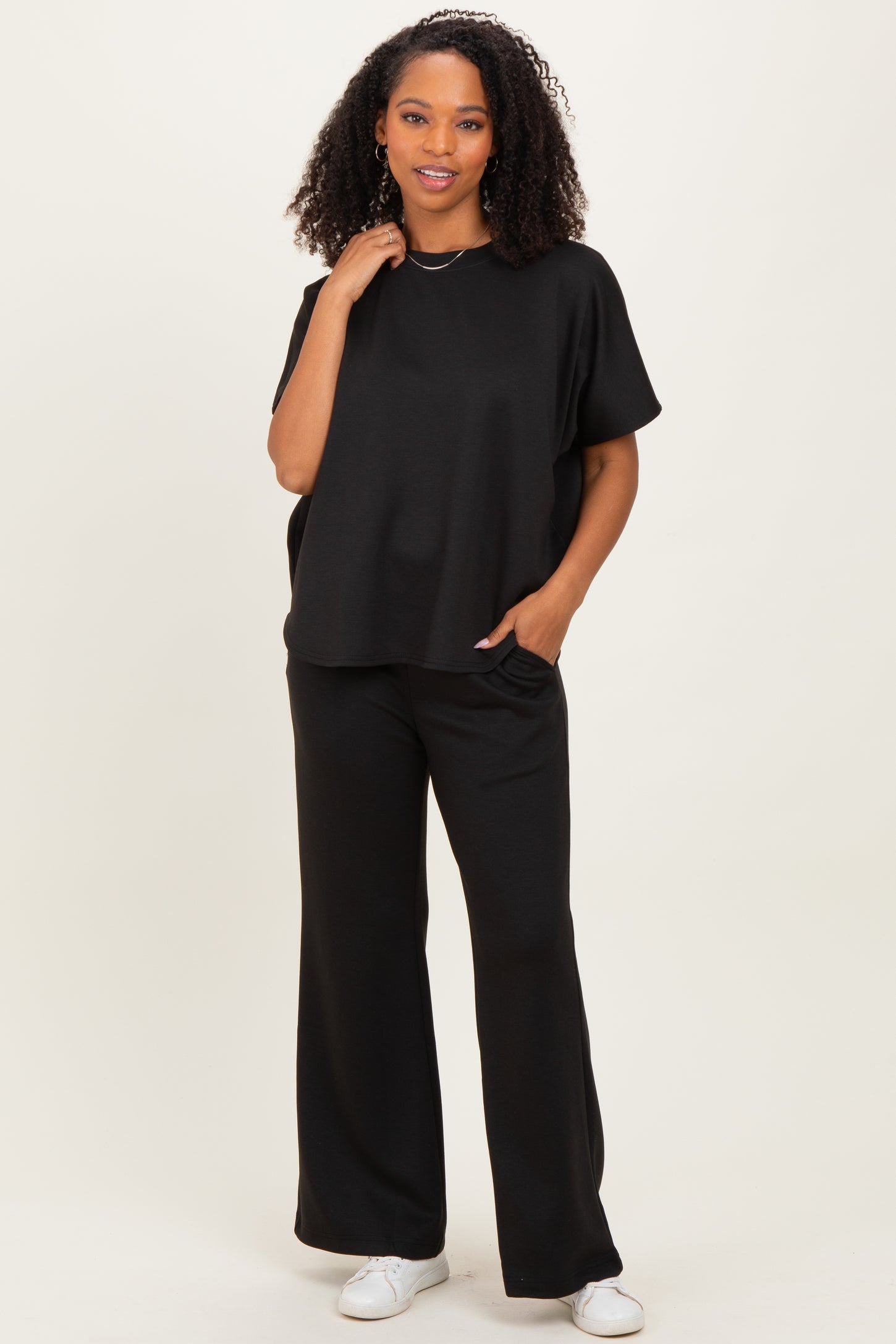 woman wearing a black oversized short sleeve top with wide leg black pants and white sneakers