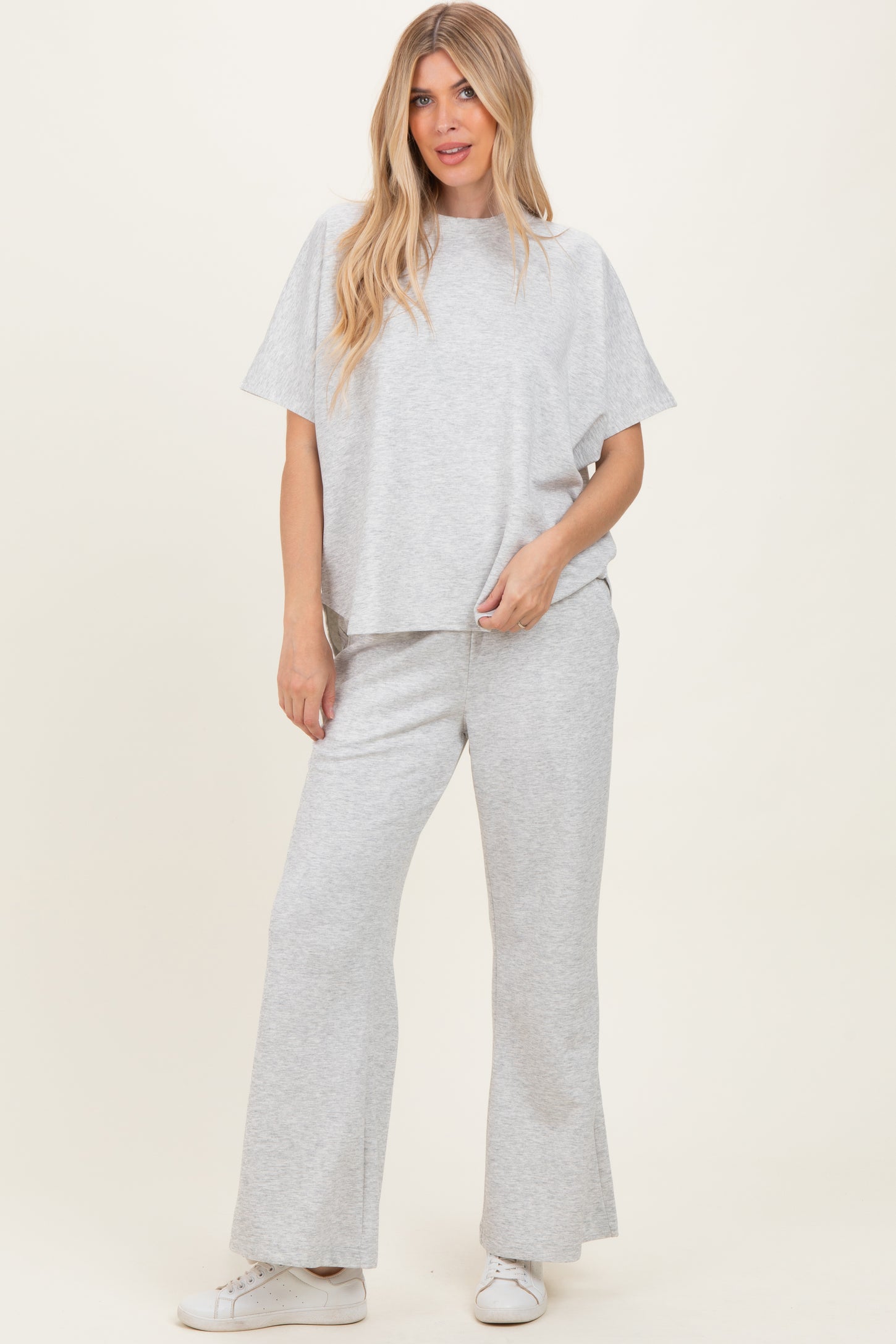 woman wearing a light grey matching lounge set with a loose top and flared pants, styled casually with white sneakers