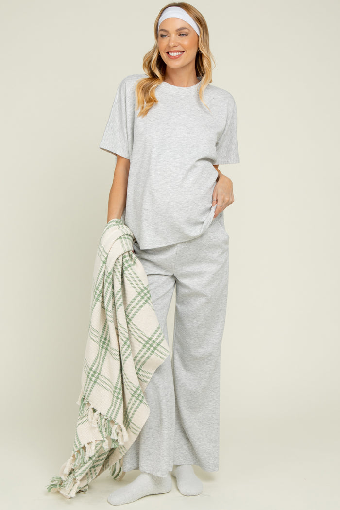 woman wearing a gray maternity pajama set with wide leg pants, holding a blanket and showing her baby bump