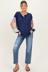 woman wearing a navy blue maternity top with patterned long sleeves and distressed jeans, smiling and standing confidently