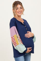 woman wearing a navy blue maternity top with colorful patterned sleeves and holding her baby bump