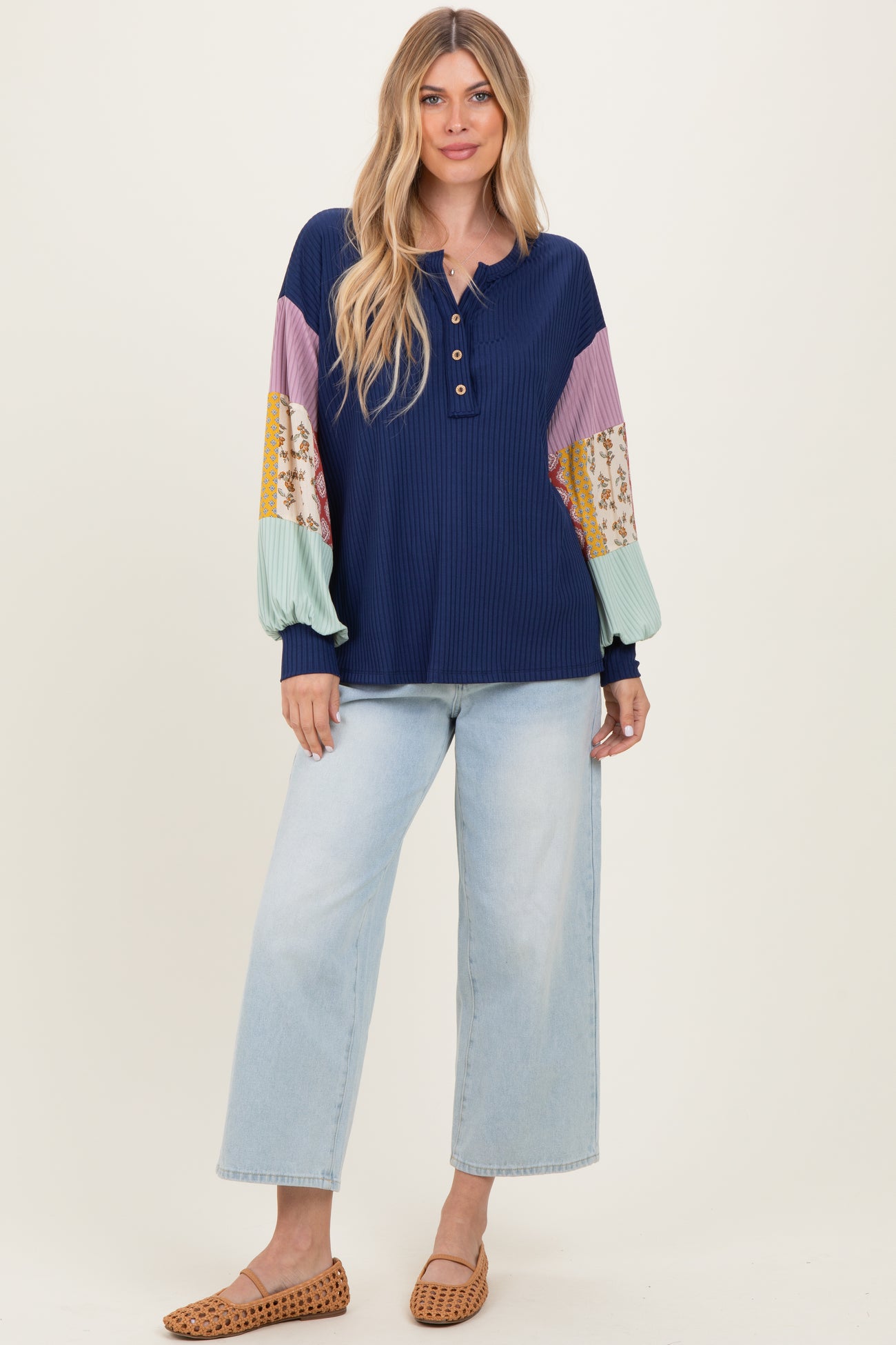 woman wearing a navy ribbed henley top with multicolored balloon sleeves and light blue wide-leg jeans