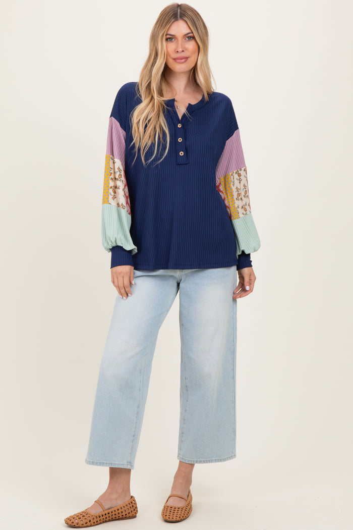 woman wearing a navy ribbed henley top with multicolored balloon sleeves and light blue wide-leg jeans