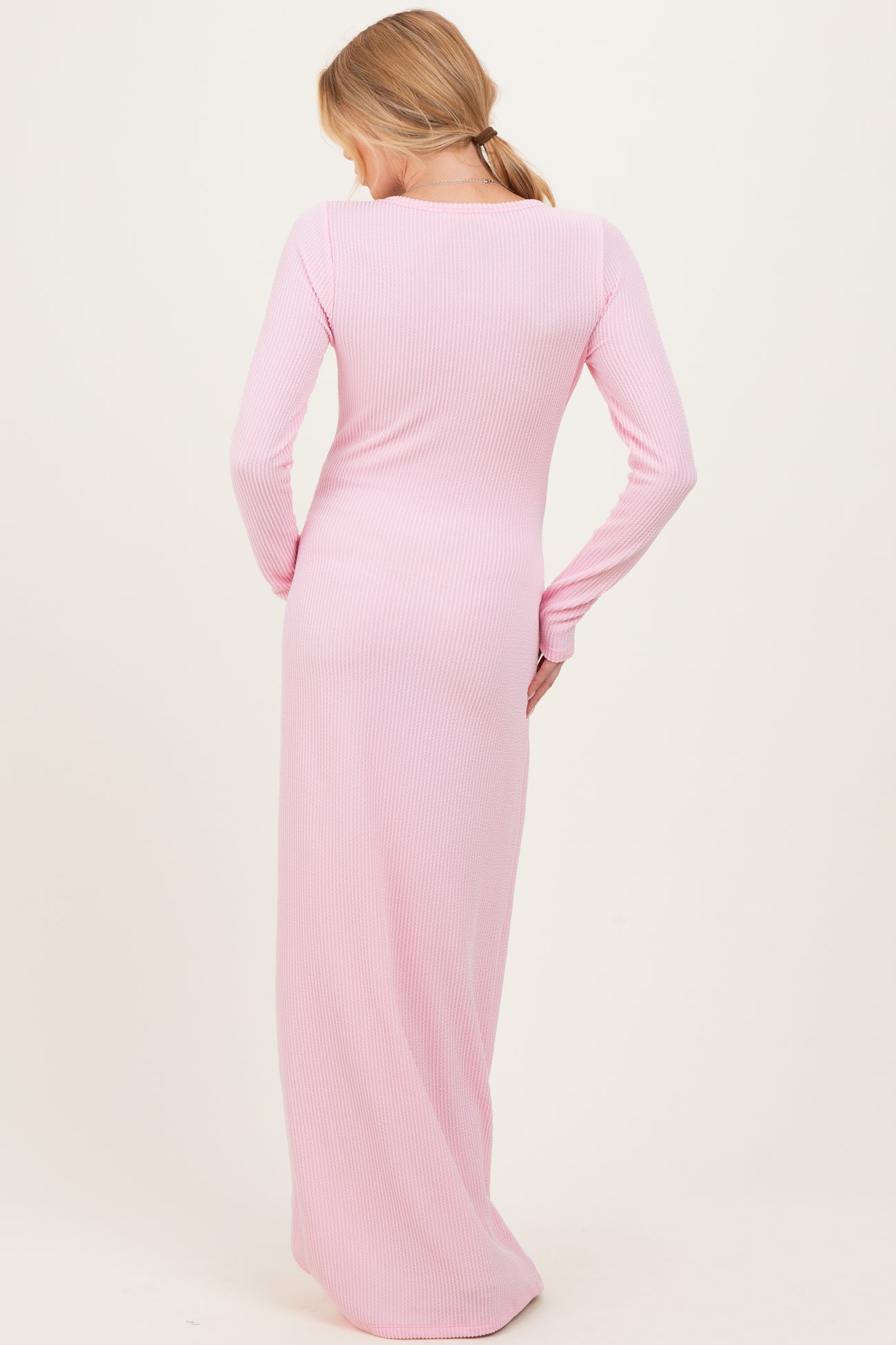 woman wearing a long pink ribbed maternity dress, showing the back view and a fitted silhouette