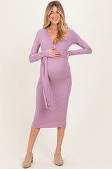 woman wearing a lavender long sleeve maternity dress with a deep v-neck and side tie, holding her baby bump