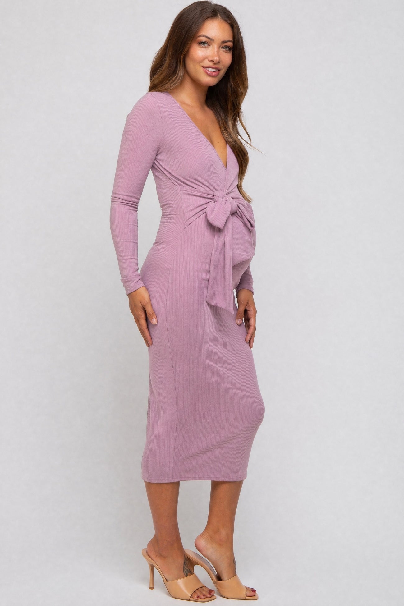 woman wearing a mauve long sleeve maternity dress with a tie detail at the waist and a visible baby bump