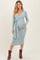 woman wearing a light teal maternity dress with a tie waist and long sleeves, holding her baby bump