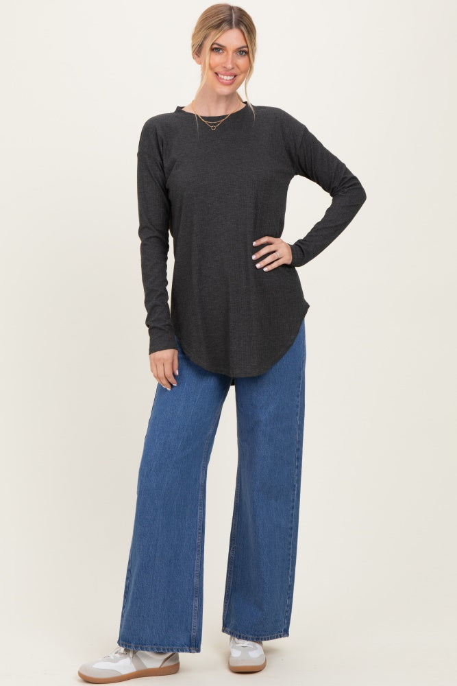 woman wearing a dark gray long sleeve top with a rounded hem and blue wide-leg jeans, standing and smiling
