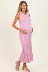woman wearing a pink ribbed maternity dress, highlighting her baby bump, with a flared hem and sleeveless design
