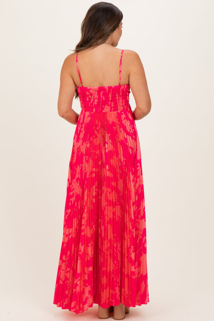 woman wearing a pink and coral patterned maternity maxi dress with a smocked bodice and pleated skirt, showing a baby bump