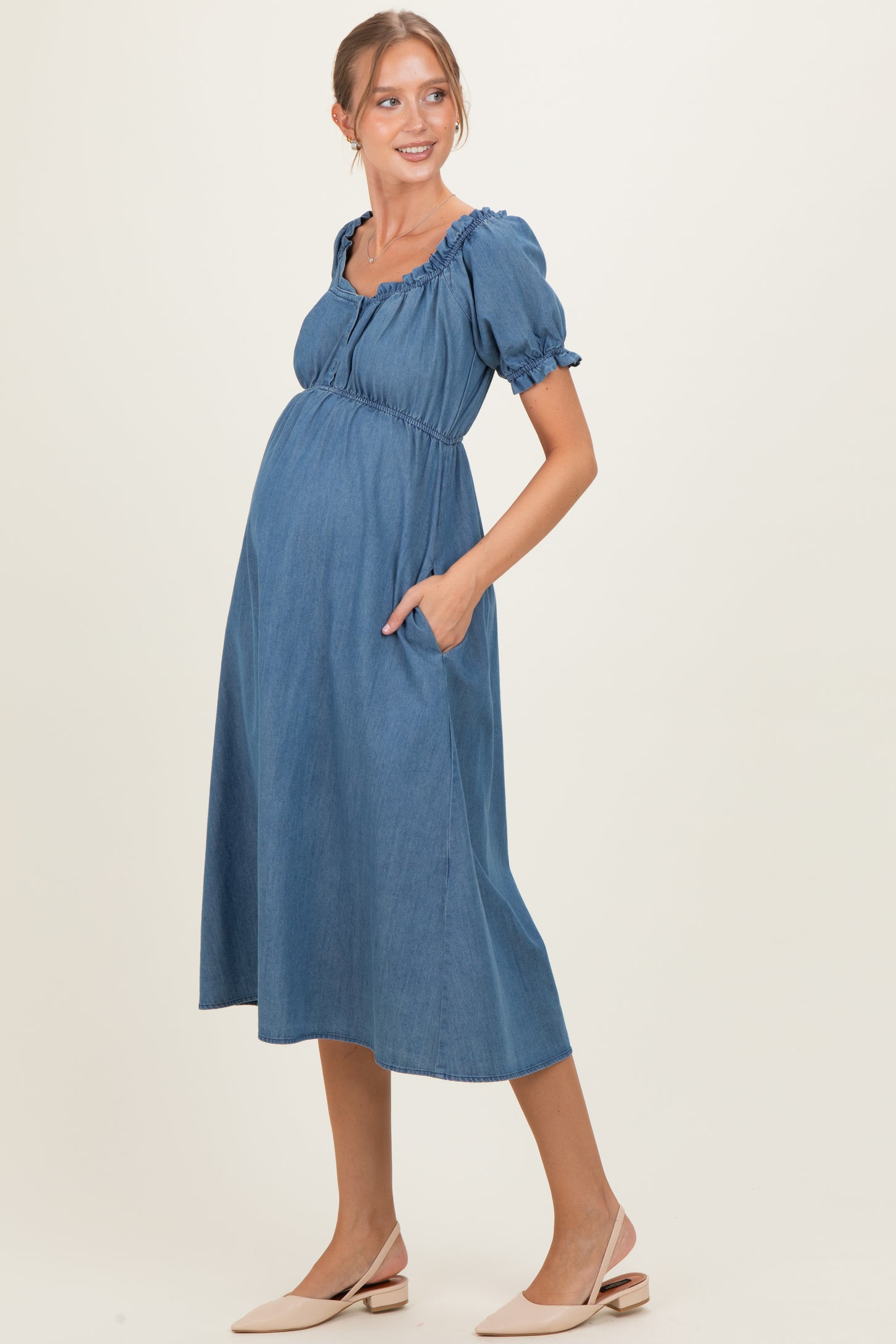 woman wearing a denim blue maternity dress with puff sleeves and pockets, highlighting her baby bump