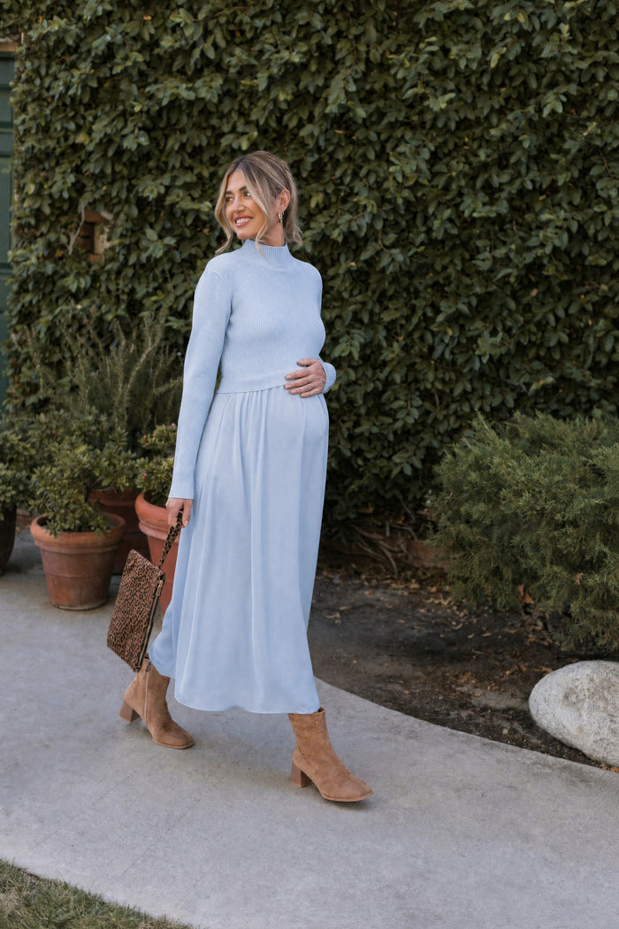 woman wearing a light blue maternity knit sweater and a flowy light blue maternity maxi skirt, holding her baby bump