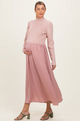 woman wearing a pink maternity dress with a ribbed high-neck top and flowing skirt, cradling her baby bump