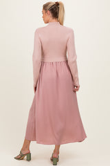 woman wearing a pink maternity dress with a ribbed top and flowing skirt, showing her back and styled with green heels