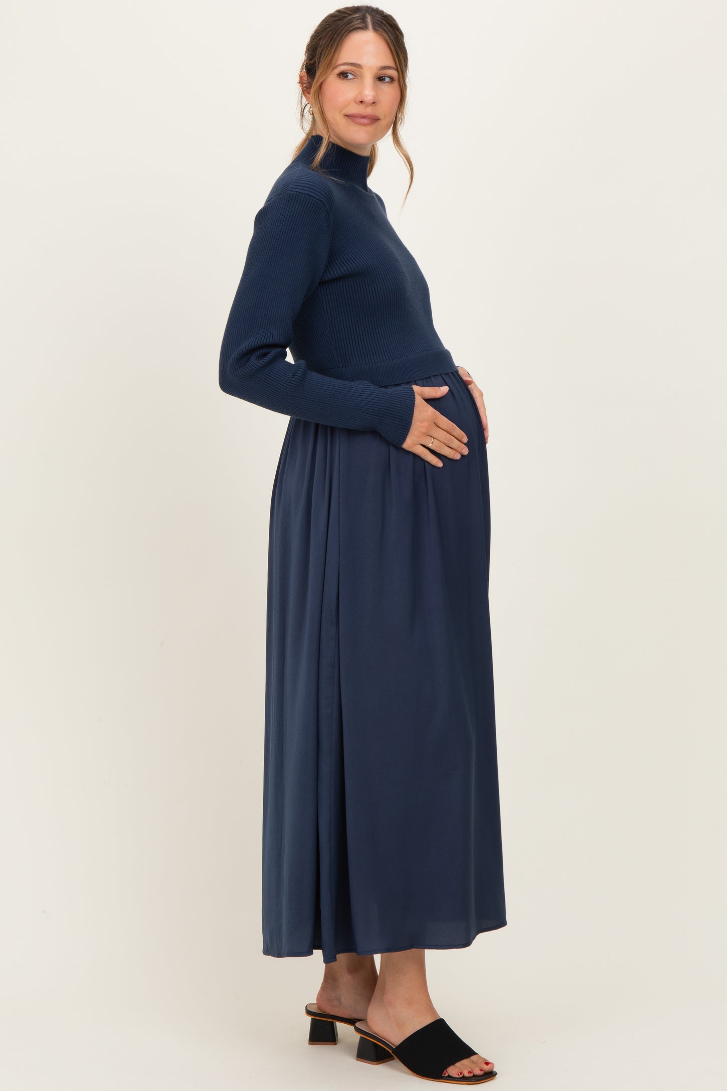 woman wearing a navy blue maternity maxi dress with a ribbed long sleeve top and a flowing skirt, gently cradling her baby bump