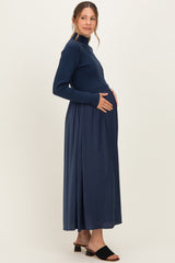 woman wearing a navy blue maternity maxi dress with a ribbed long sleeve top and a flowing skirt, gently cradling her baby bump