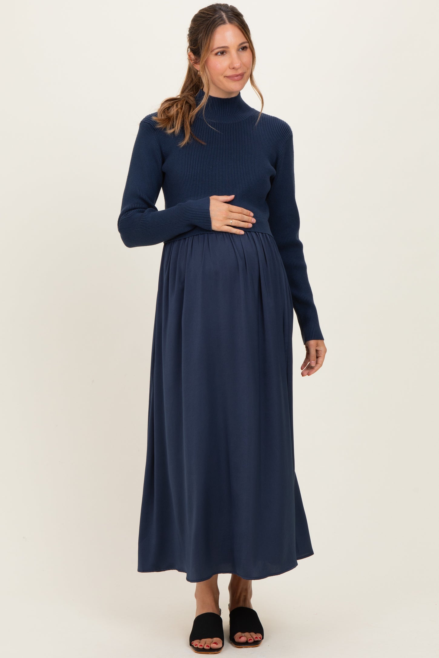 woman wearing a navy blue long sleeve maternity dress with a fitted top and flowing skirt, holding her baby bump