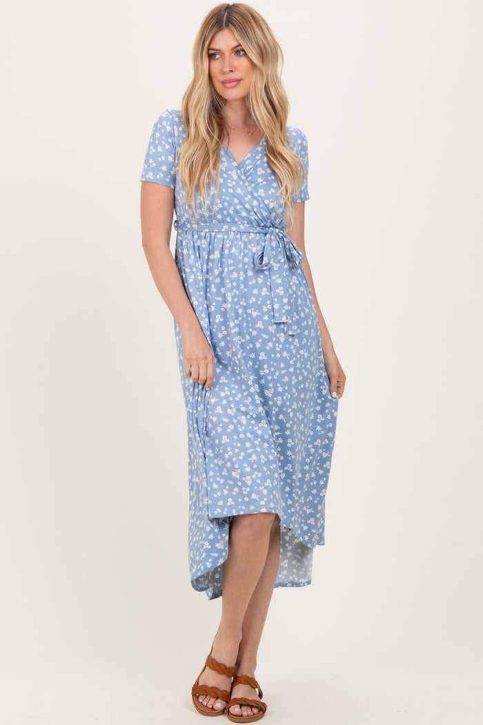 woman wearing a blue floral wrap dress with short sleeves and a tie waist, standing against a neutral background