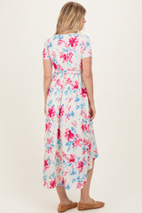 woman wearing a floral print maxi dress in pink and blue with short sleeves and a high-low hemline.