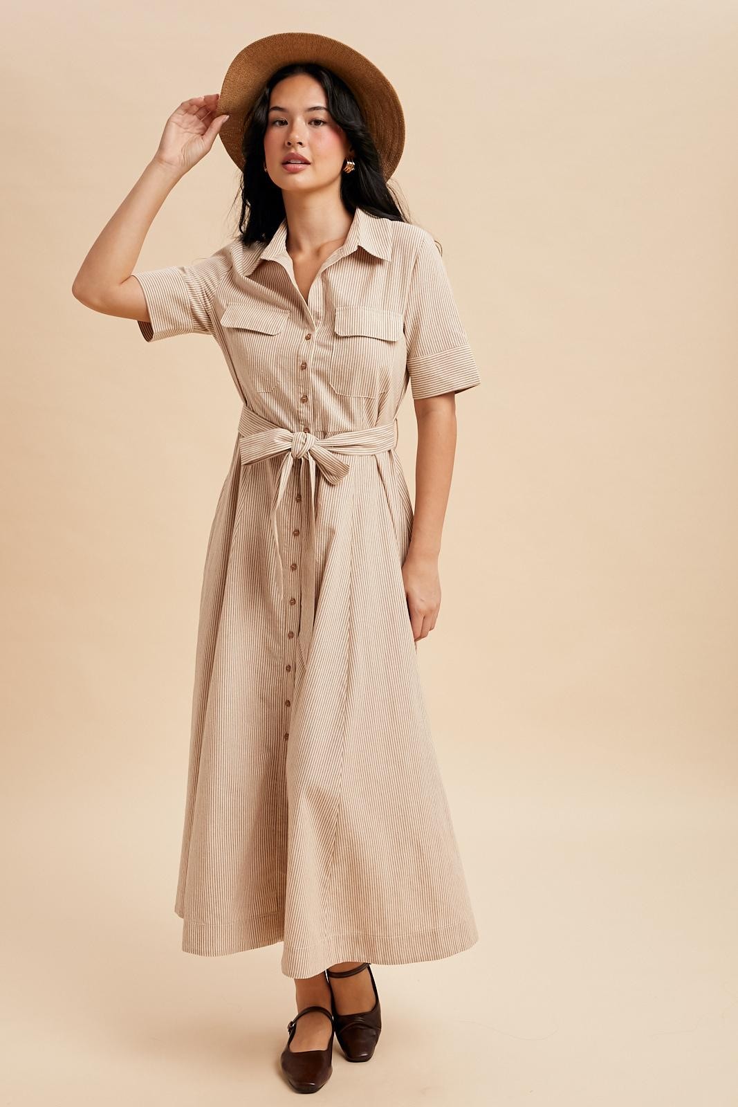 woman wearing a beige striped midi shirt dress with a tie waist and short sleeves, styled with a wide-brimmed hat